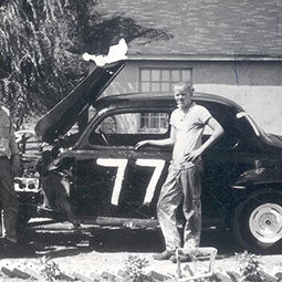 A old black and white photo of a young Randy Sweet standing in front of a old Ford race car.