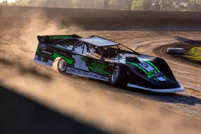 A race car in the middle of a turn on a dirt race track.