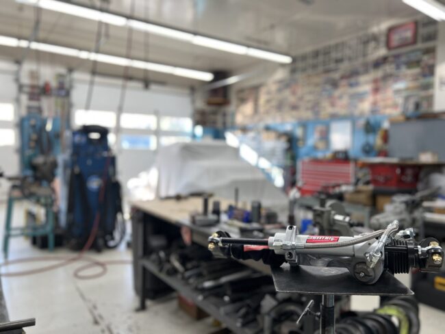 A Sweet Manufacturing, Inc. rack & pinion component part sits on a cart, focused on by the camera with a blurry machine shop in the background.