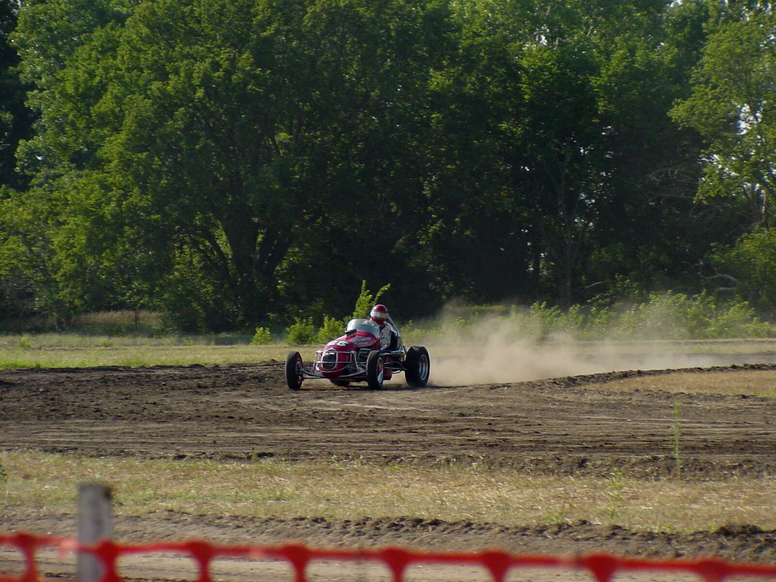A midget car drives down a dirt track.