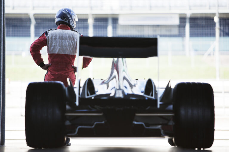 Racer standing with car in garage A race car driver stands in front of a race car parked in a garage.