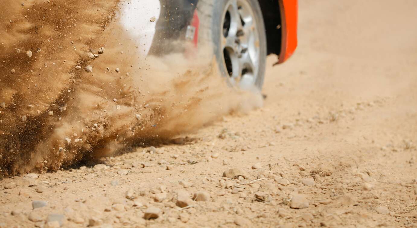 Close-up of a red race car's tire spraying dirt while driving down a dirt track.
